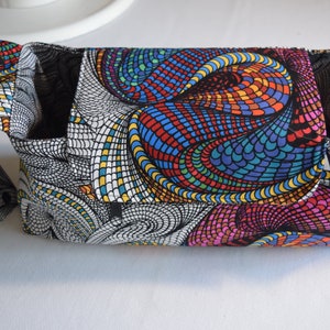 May include: A fabric crossbody bag featuring a vibrant, multi-colored mosaic pattern of swirling, interconnected shapes in shades of red, blue, yellow, and green, contrasted with sections of black and white geometric line work and black snap closures.