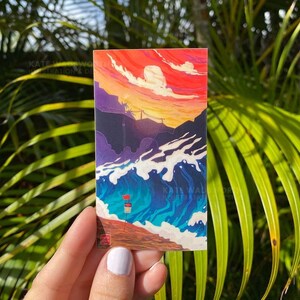 May include: A sticker featuring a colorful illustration of a sunset over a beach with waves crashing on the shore. The sky is a vibrant red and orange with white clouds. The water is a deep blue with white foam. There are two red flags on the beach.