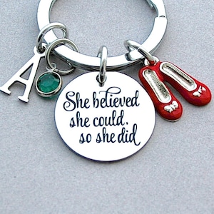May include: A silver keyring with a charm that says "She believed she could. So she did." The charm is attached to a silver ring with a green gem and a silver letter A. There are also two red shoe charms attached to the ring.