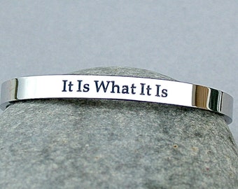 May include: A silver bracelet with the words "It Is What It Is" engraved on it.