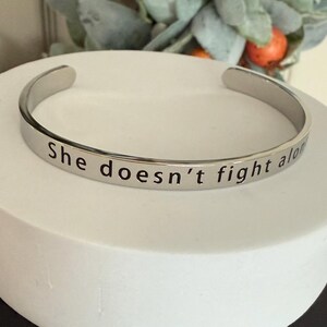 May include: Silver bangle bracelet with the inscription "She doesn't fight alone".