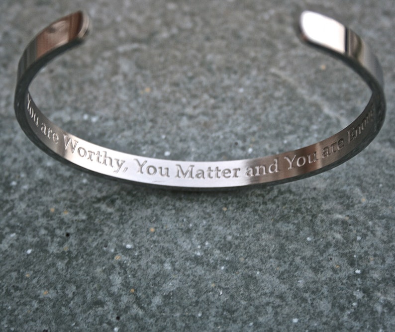 May include: A silver bangle bracelet with the inscription "You are Worthy, You Matter and You are Loved".