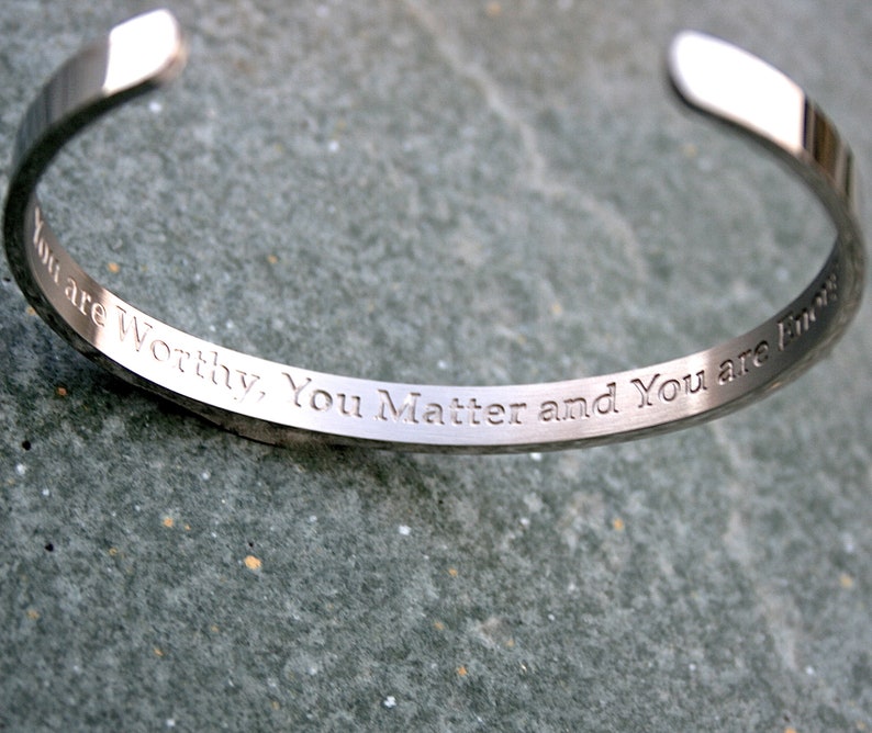 May include: A silver bangle bracelet with the inscription "You are Worthy, You Matter and You are Fine".