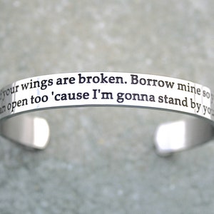 May include: Silver cuff bracelet with the inscription "If your wings are broken. Borrow mine so you can open too 'cause I'm gonna stand by you."
