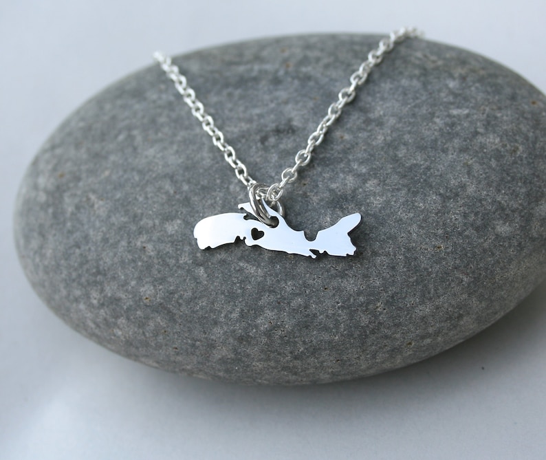 May include: A silver necklace with a pendant shaped like the island of Prince Edward Island, Canada. The pendant has a small heart cutout in the center.