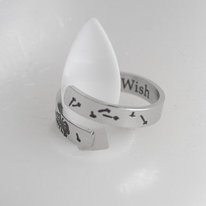 May include: Silver adjustable ring with the word "Wish" engraved on the band. The ring also features a small engraved design of a dandelion with seeds blowing in the wind.