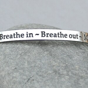 May include: Silver bracelet with the inscription "Breathe in - Breathe out - Move"