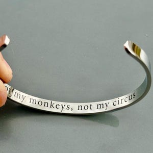 May include: Silver bangle bracelet with the inscription "Not my monkeys, not my circus".