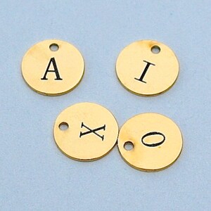 May include: Four gold-coloured metal discs with letters and symbols engraved on them. The letters are A, I, X, and a circle.