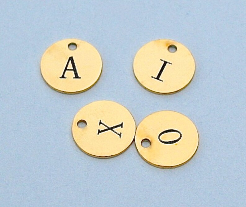 May include: Four gold-coloured metal discs with letters and symbols engraved on them. The letters are A, I, X, and a circle.