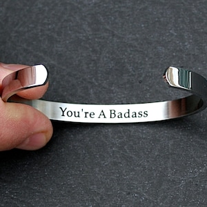May include: A silver bracelet with the words "You're A Badass" engraved on it.
