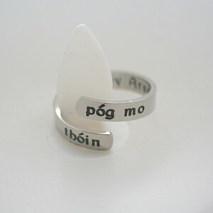 Peut inclure: Une bague en argent avec les mots "póg mo thóin" gravés dessus. La bague est une bande simple avec un design légèrement incurvé.