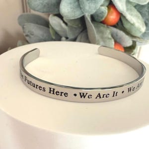 May include: Silver bracelet with the inscription "The Futures Here - We Are It - We Are"