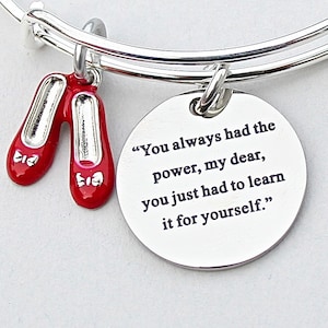 May include: Silver charm bracelet with a red ruby slipper charm and a round charm with the quote "You always had the power, my dear, you just had to learn it for yourself."