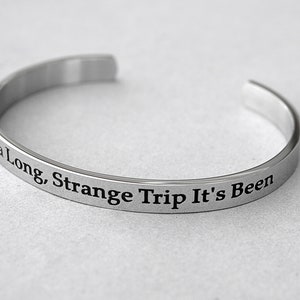 May include: A silver bangle bracelet with the inscription "What a Long, Strange Trip It's Been."