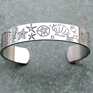 May include: A silver bracelet featuring a design of various sea creatures and objects, including a starfish, a seahorse, a seashell, and a turtle.