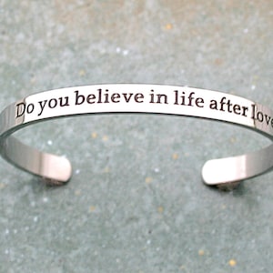 May include: A silver bangle bracelet with the inscription "Do you believe in life after love" engraved on the front.