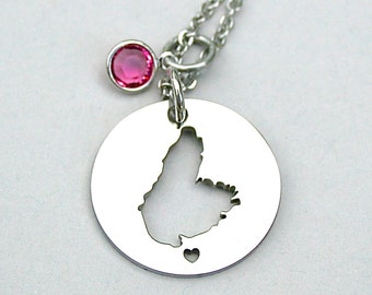 May include: A silver necklace with a pendant shaped like the island of Barbados. The pendant has a small heart cut out of it. The necklace has a pink crystal charm.