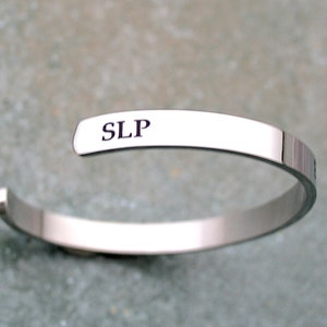 May include: A silver bangle bracelet with the inscription "SLP" engraved on the front.