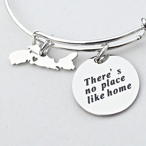 May include: Silver charm bracelet with a charm shaped like Prince Edward Island and a round charm with the text "There's no place like home".