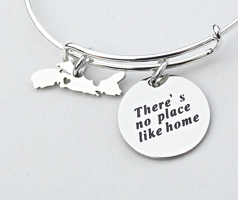 May include: Silver charm bracelet with a charm shaped like Prince Edward Island and a round charm with the text "There's no place like home".