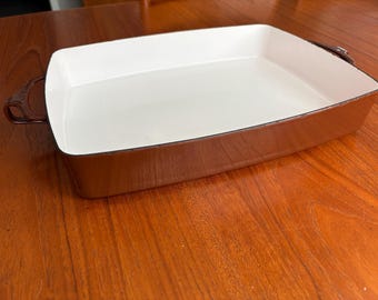 Op de afbeelding: Een rechthoekige bruine ovenschaal met een witte binnenkant. De schaal heeft afgeronde hoeken en twee handvatten. De ovenschaal is gemaakt van duurzaam materiaal en is geschikt voor het bakken van diverse gerechten.