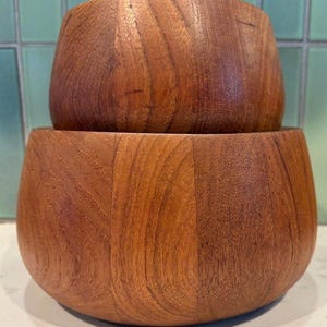 以下が含まれることがあります： 積み重ねられた2つの木製のボウル。ボウルは暖色系の木材で作られており、木目がはっきりと見えます。ボウルは丸みを帯びた形状で滑らかな仕上がりで、サービングやディスプレイに適しています。