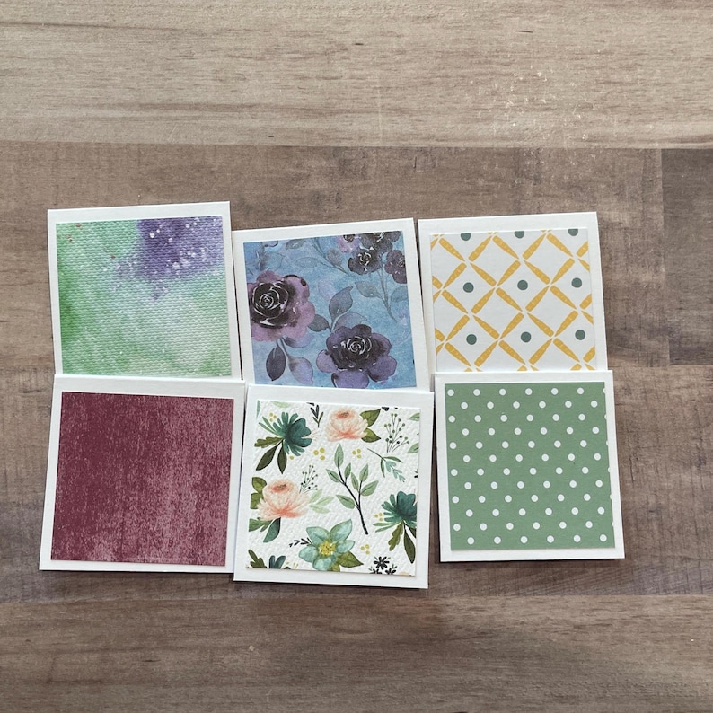 May include: A collection of six square cards with various patterns. The patterns include watercolor textures, floral designs, and geometric shapes in colors like purple, burgundy, green, and yellow. Each card has a white border.