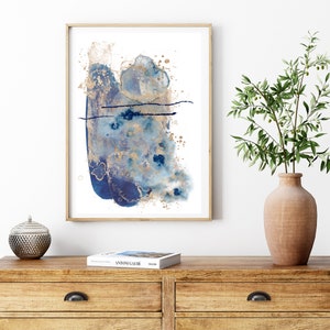 May include: Abstract art print featuring blue and gold watercolour paint splatters on a white background. The print is framed in a natural wood frame.