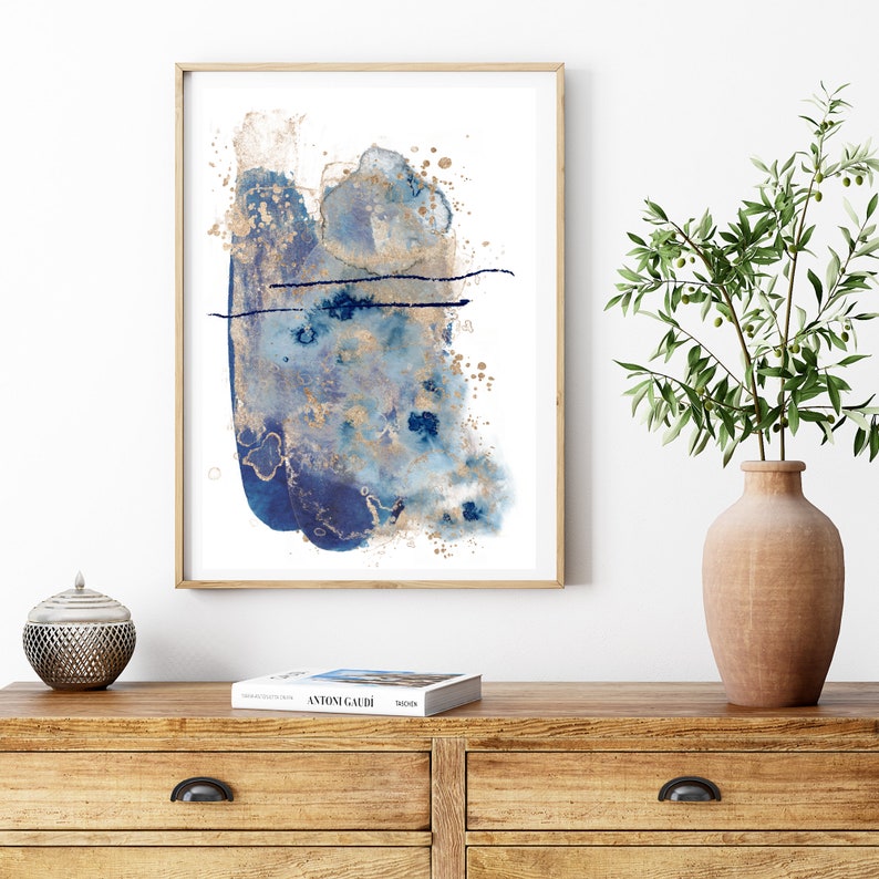 May include: Abstract art print featuring blue and gold watercolour paint splatters on a white background. The print is framed in a natural wood frame.