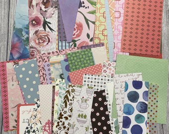 May include: A collection of rectangular paper strips featuring diverse patterns including floral prints, polka dots, geometric shapes, watercolor circles, and botanical illustrations of potted plants, with some pieces displaying handwritten script text.