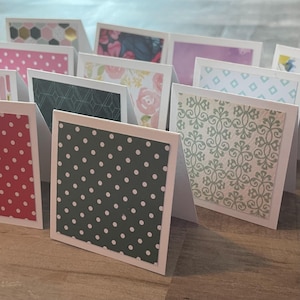 May include: A collection of handmade greeting cards with various patterned designs. The cards feature white borders and are decorated with polka dots, floral prints, geometric shapes, and decorative patterns in shades of green, pink, and white.