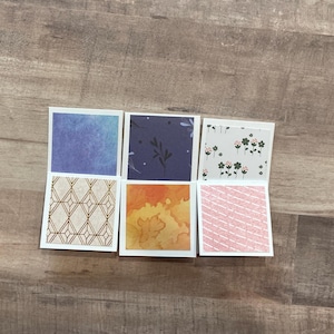 May include: Six small, square cards with decorative patterns. The top row features a blue watercolor, a navy floral, and a white floral design. The bottom row shows a gold geometric, an orange watercolor, and a pink diagonal stripe pattern.