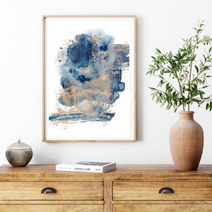 May include: Abstract watercolour painting in shades of blue and gold. The painting features a large, abstract shape in the centre, with smaller shapes and details surrounding it. The painting is framed in a simple, wooden frame.