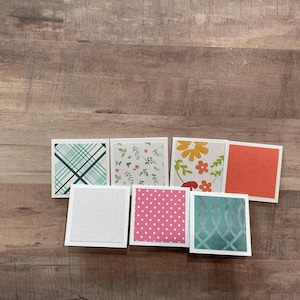 May include: A collection of square cards with various patterns. Designs include teal plaid, floral, polka dots, and geometric patterns in colors like pink, orange, and teal. Each card has a white border.