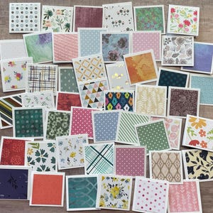 May include: A collection of small, square cards with various patterns and designs. The cards feature floral, geometric, and abstract patterns in a variety of colors, including pink, blue, green, and yellow. Each card has a white border.
