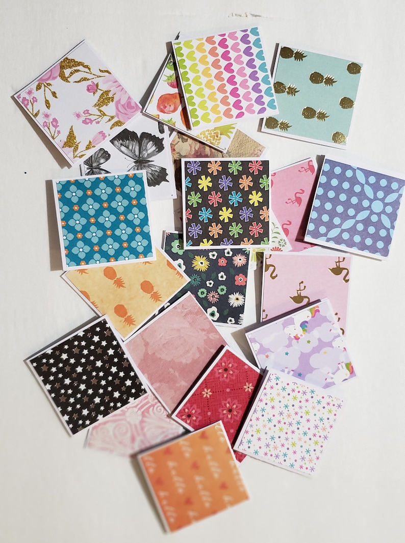 Op de afbeelding: Assortiment van 16 kleine vierkante kaartjes met verschillende patronen. De patronen omvatten ananas, harten, sterren, bloemen en geometrische ontwerpen. De kaartjes zijn wit met een witte rand.