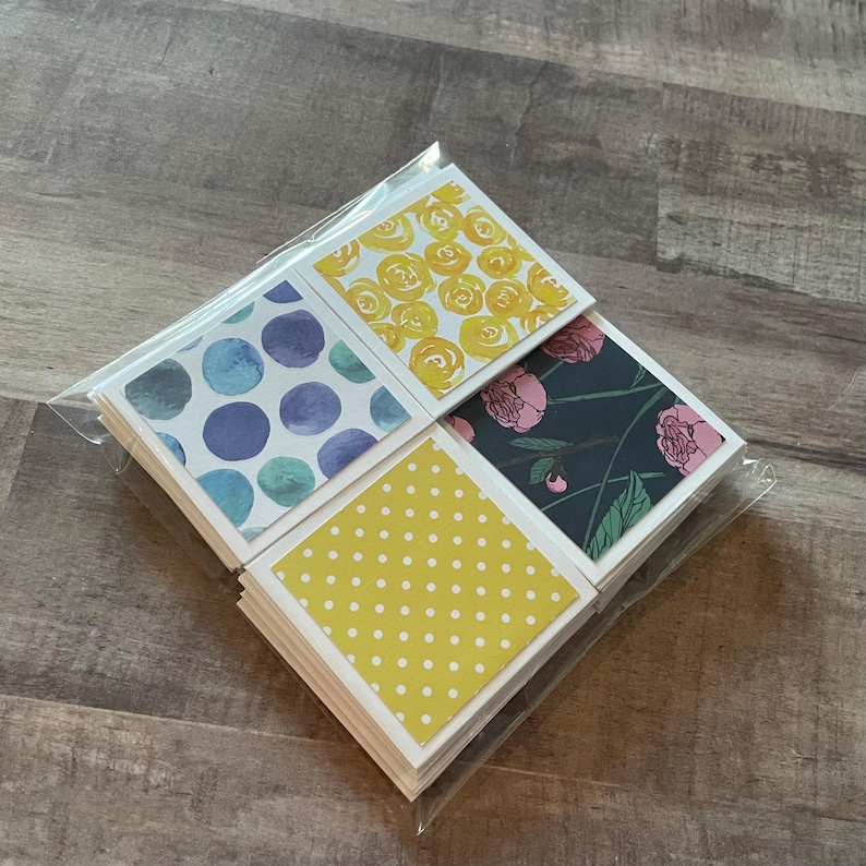 May include: A stack of square cards with various designs, including yellow roses, blue watercolor circles, pink floral patterns, and yellow polka dots. The cards are packaged in a clear plastic sleeve.