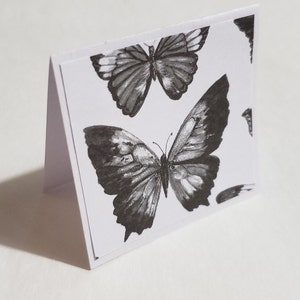 Op de afbeelding: Een witte kaart met een zwart-witte vlinderontwerp. De vlinder heeft ingewikkelde details en is in aquarelstijl.
