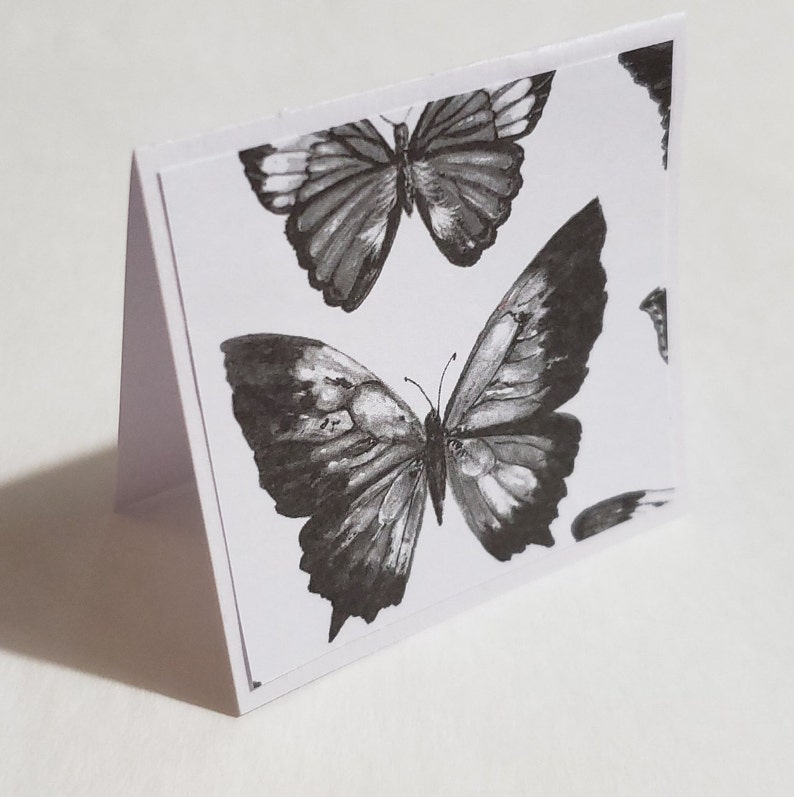Op de afbeelding: Een witte kaart met een zwart-witte vlinderontwerp. De vlinder heeft ingewikkelde details en is in aquarelstijl.
