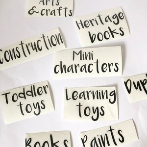 May include: A set of nine white labels with black text, each with a different label for a storage bin. The labels include: Arts & Crafts, Construction, Heritage Books, Mini Characters, Toddler Toys, Learning Toys, Books, Paints, and Dup.