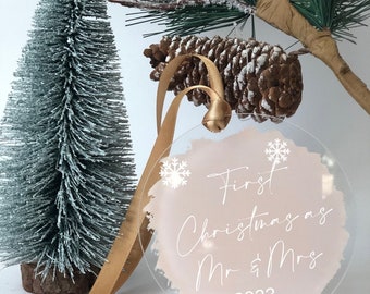 May include: A round, clear acrylic Christmas bauble with a pink watercolour background. The bauble has white snowflakes and the text "First Christmas as Mr & Mrs 2023" in white.