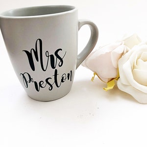 May include: A gray ceramic mug with a black cursive inscription that reads "Mrs. Preston".