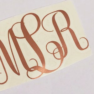 May include: A rose gold monogram sticker with the letters "MPR" in a cursive font.