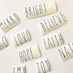 May include: A set of ten white vinyl stickers with black lettering. The words on the stickers are: Merry, Bright, Believe, Love, Hope, Joy, Faith, Amy, Nat, and AC.