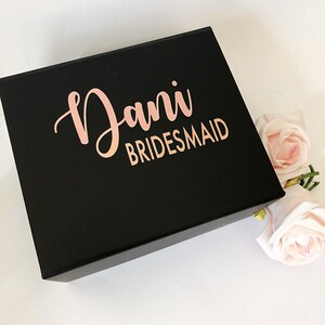 May include: A black gift box with the name "Dani Bridesmaid" written in rose gold lettering.