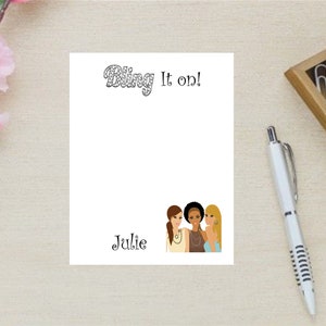 May include: A white notepad with the text "Bling It On!" at the top and the name "Julie" written below. Three women with different hairstyles and jewelry are pictured at the bottom.