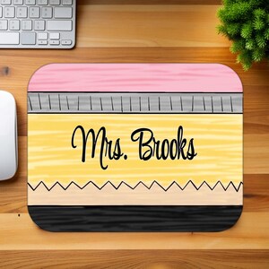 May include: A yellow and pink pencil-shaped mouse pad with a black eraser and the text "Mrs. Brooks" in black.