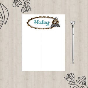 May include: A white notepad with a leopard print border and a teal oval with the name "Haley" written in it. A small leopard print design is on the right side of the oval. A silver pen is on the right side of the notepad.