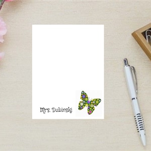 May include: A white card with a colorful butterfly design and the text "Mrs. Dubinski" printed on it.